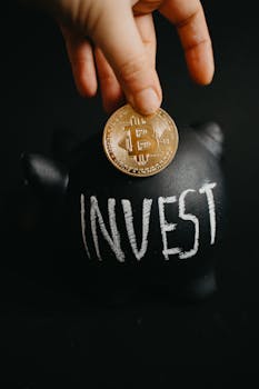 Gold bitcoin inserted into a black piggy bank labeled 'Invest', symbolizing cryptocurrency saving.